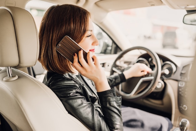 Beautiful woman is talking on the mobile phone and smiling while sitting in the car