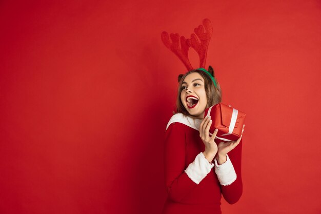 Beautiful woman like christmas deer isolated on red wall 