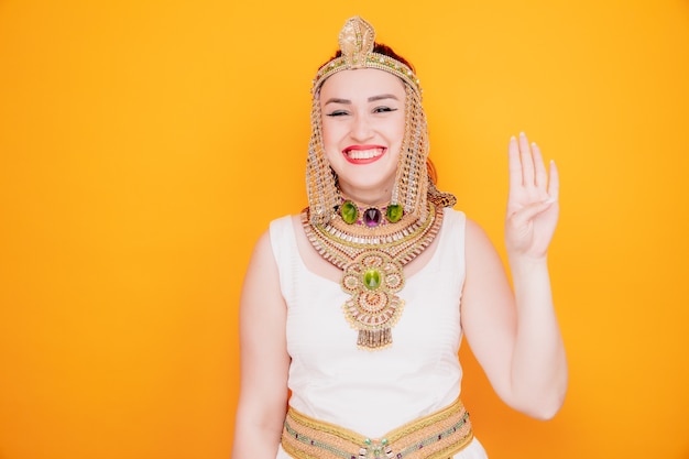 Beautiful woman like cleopatra in ancient egyptian costume happy and cheerful smiling showing number four with fingers on orange