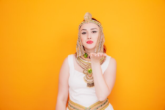 Beautiful woman like cleopatra in ancient egyptian costume happy and positive sending air kiss on orange