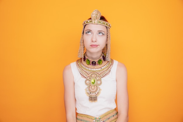 Beautiful woman like cleopatra in ancient egyptian costume loking up being unhappy and displeased making wry mouth on orange