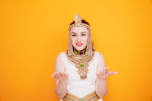 Beautiful woman like cleopatra in ancient egyptian costume raising hands in displeasure on orange