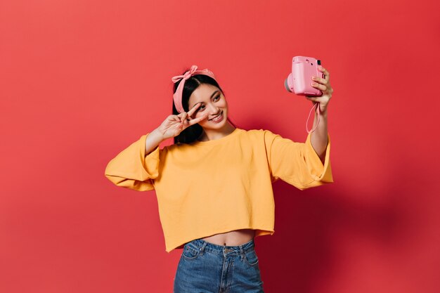 Beautiful woman in orange sweater and jeans shows peace sign and makes selfie