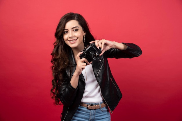 Beautiful woman photographer holding photo camera on a red background. High quality photo