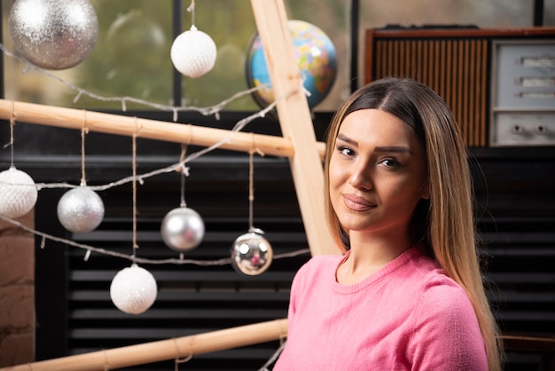 Free photo beautiful woman in pink sweater posing over christmas lights.