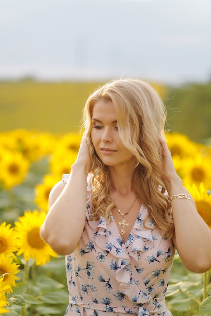 Beautiful woman poses in the agricultural field with sunflower on a sunny summer day