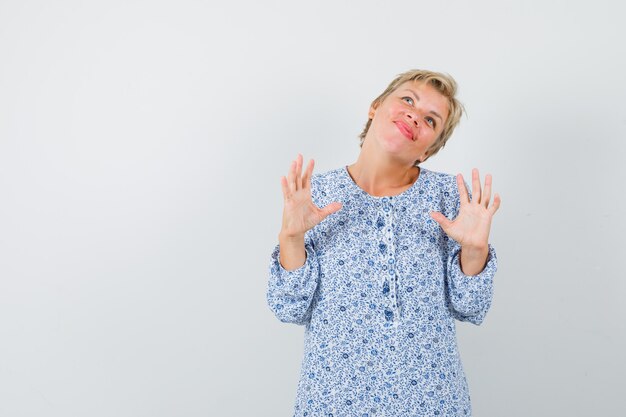 Beautiful woman raising hand to defend herself in patterned blouse front view.