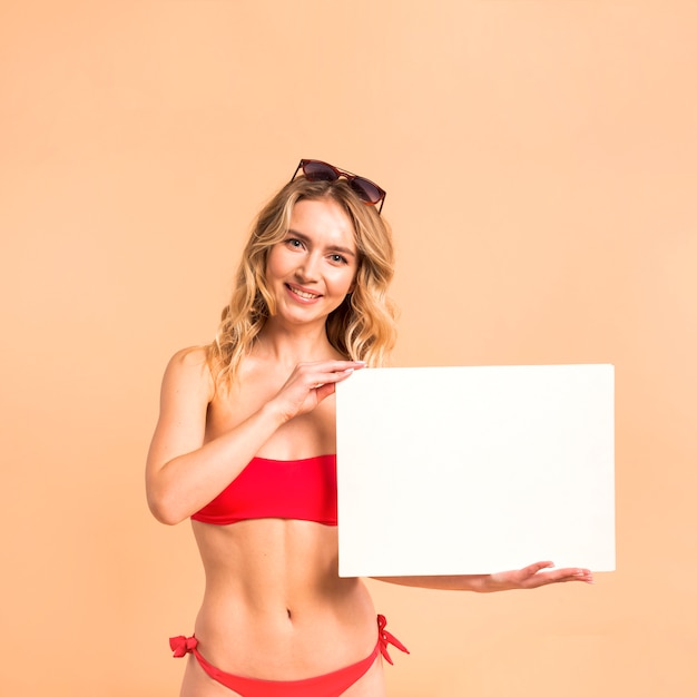 Free photo beautiful woman in red swimsuit showing blank paper