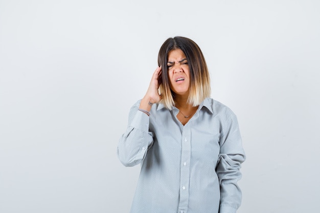 Beautiful woman rubbing temples, feeling headache in shirt and looking distressed , front view.