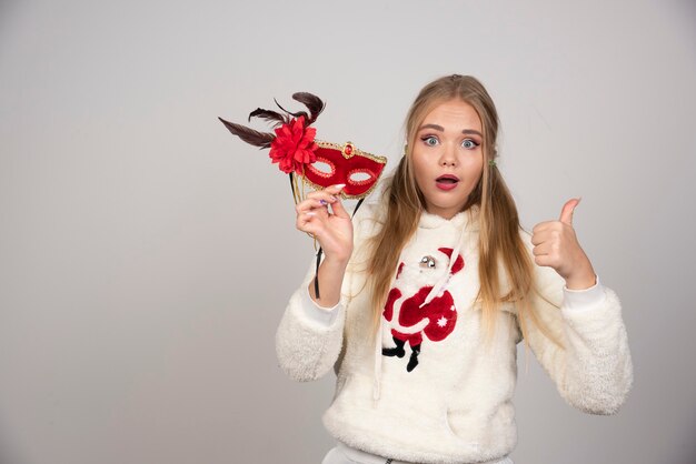 Beautiful woman showing masquerade mask and giving thumbs up.