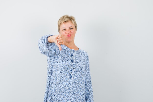 Beautiful woman showing thumb down in patterned blouse and looking displeased. front view.