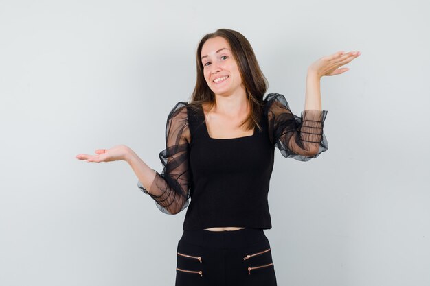 Beautiful woman spreading open palms aside in black blouse and looking cheery. front view.