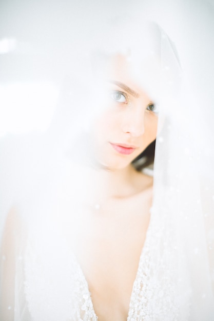 Beautiful woman standing and looking in room with white in long white dress.