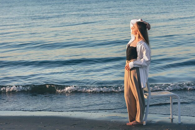 A beautiful woman stands near the sea at sunset