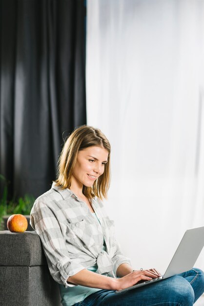 Beautiful woman using laptop near sofa