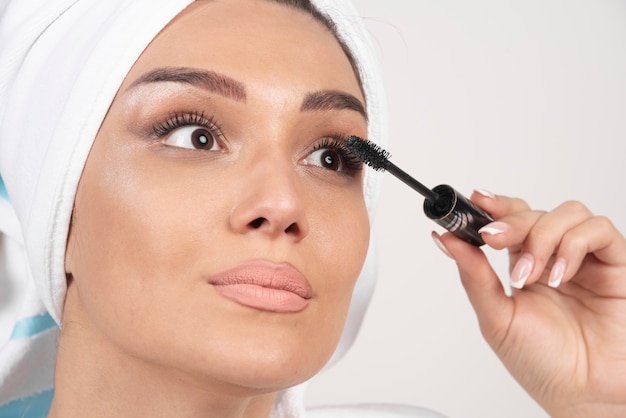 Beautiful woman using mascara in towel on a white background.