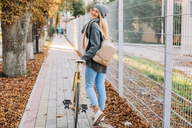 Beautiful woman walking with bicycle near fence