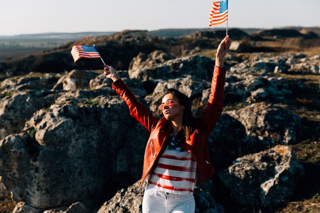 Free Photo beautiful woman waving american flags on rocky background