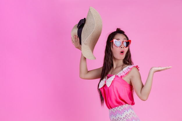 A beautiful woman wearing red glasses with a big hat on a pink .