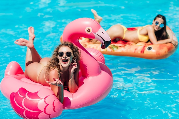 Beautiful woman, wearing swimsuit, lying on a pink flamingo air mattress in a pool of blue water, summer.