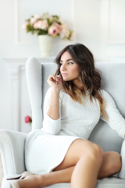 Beautiful woman wearing white dress and sitting in white armchair