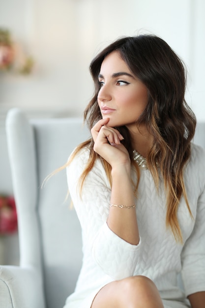 Beautiful woman wearing white dress and sitting in white armchair