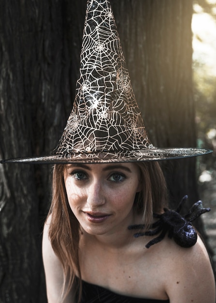 Beautiful woman in witch hat looking at camera with decorative spider sitting on shoulder