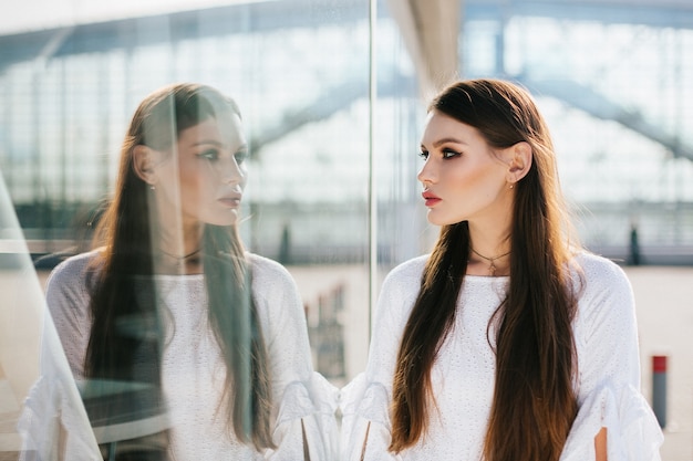 Free photo beautiful woman with long hair looks at her reflection in the modern glass building