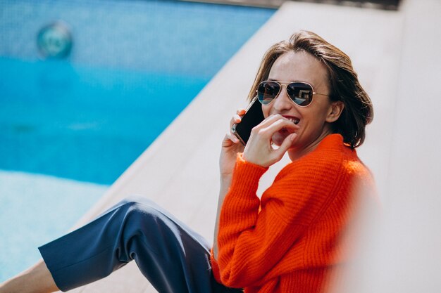 Beautiful woman with phone sitting by the pool