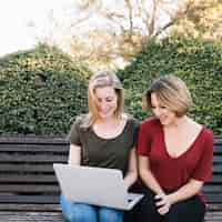 Free photo beautiful women browsing laptop on bench