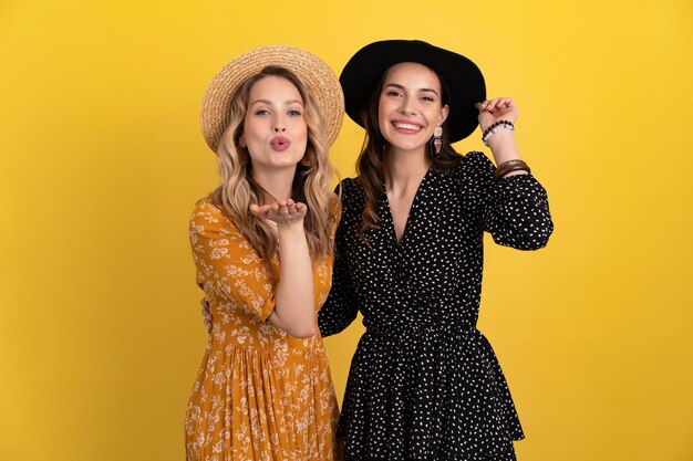 Beautiful women friends together isolated on yellow background in black and yellow dress and hat