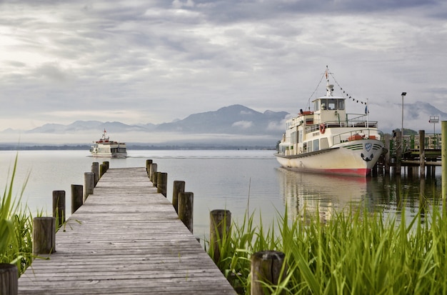 Free Photo beautiful of a wooden deck leading to the sea with mountains and ships on the background