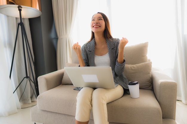 Beautiful young asian portrait using computer and laptop with coffee cup sitting on sofa