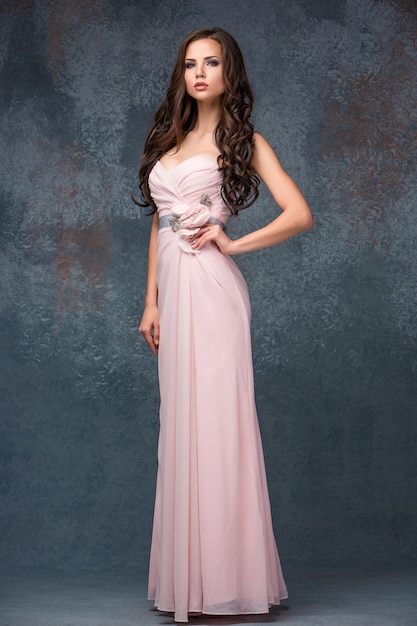 Beautiful young brunette woman with her hair posing in a i long pink dress.  