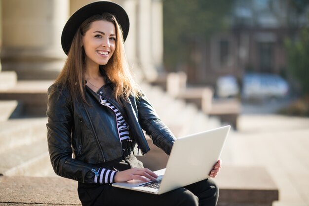 Beautiful young businesswoman girl works with her brand laptop computer in the city centre