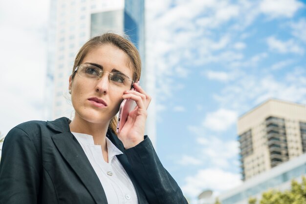 Beautiful young businesswoman talking on mobile phone standing against sky