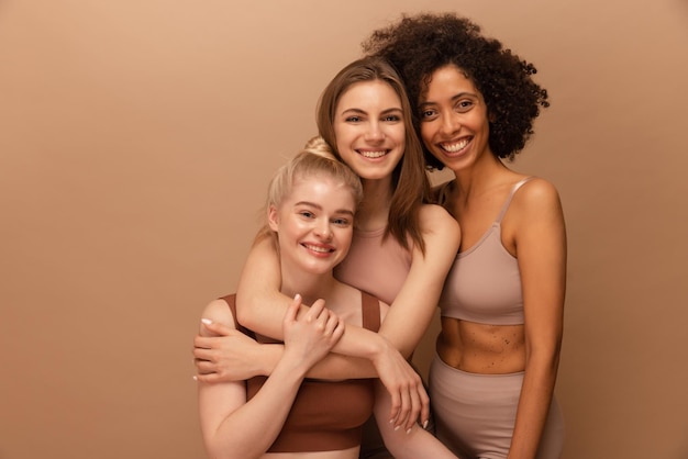 Beautiful young caucasian and african women in lingerie posing on beige background Lifestyle concept