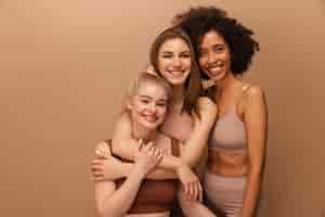 Free photo beautiful young caucasian and african women in lingerie posing on beige background lifestyle concept