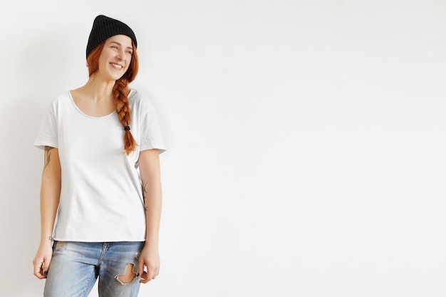 Free photo beautiful young caucasian female with ginger hair in braid standing isolated against studio wall