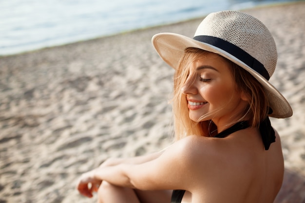 Beautiful young cheerful girl in hat rests at morning beach