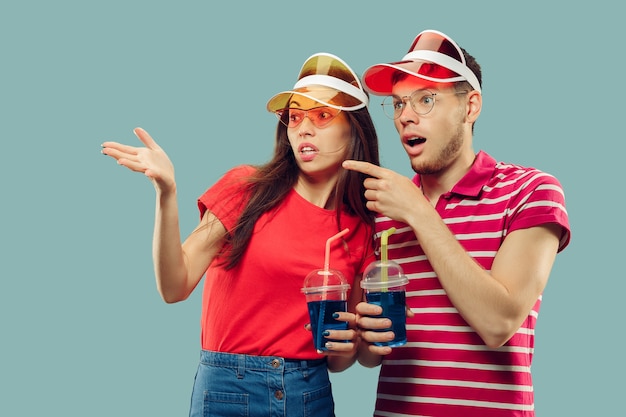 Beautiful young couple's half-length portrait isolated. Smiling woman and man in caps and sunglasses with drinks. Facial expression, summer, weekend concept. Trendy colors.