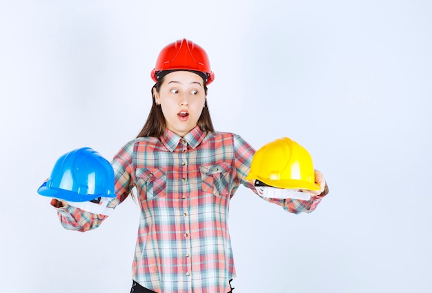 Free photo beautiful young engineer holding security helmets and standing on white background.