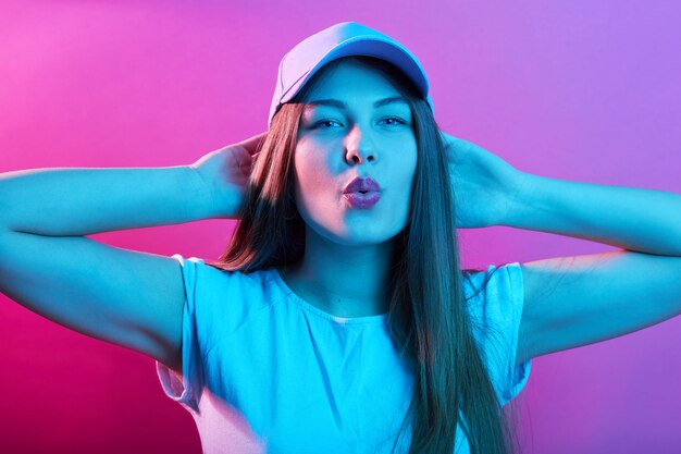 Free photo beautiful young european female in baseball cap keeping hands on neck and showing air kiss, wearing casual outfit