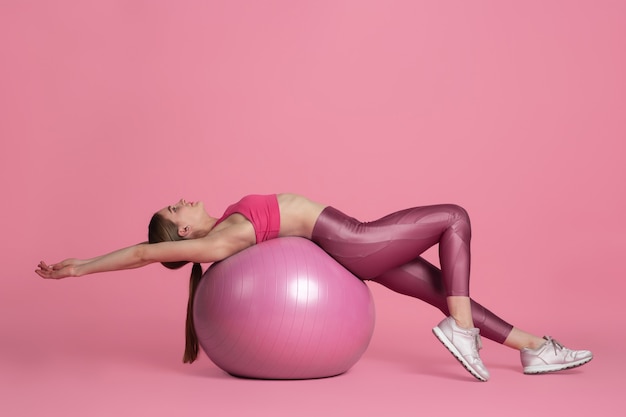 Beautiful young female athlete practicing on pink studio wall monochrome portrait