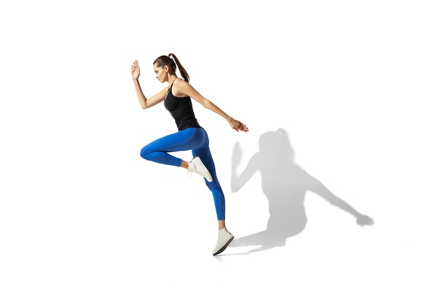 Beautiful young female athlete stretching, training on white  space, portrait with shadows