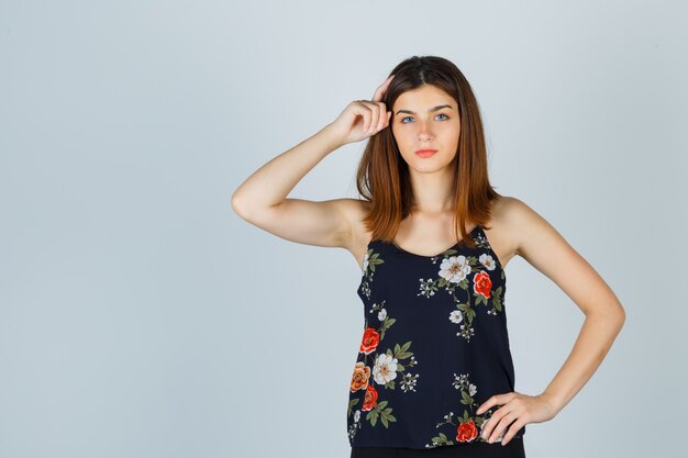 Beautiful young female holding hand on head in blouse and looking thoughtful