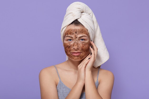 Beautiful young female with chocolate mask on face, poses with white towel on head