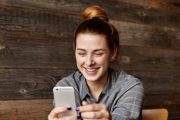 Free Photo beautiful young female with hair bun holding generic smart phone, checking newsfeed on social media