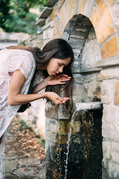 Beautiful, young girl drinks spring water outdoor