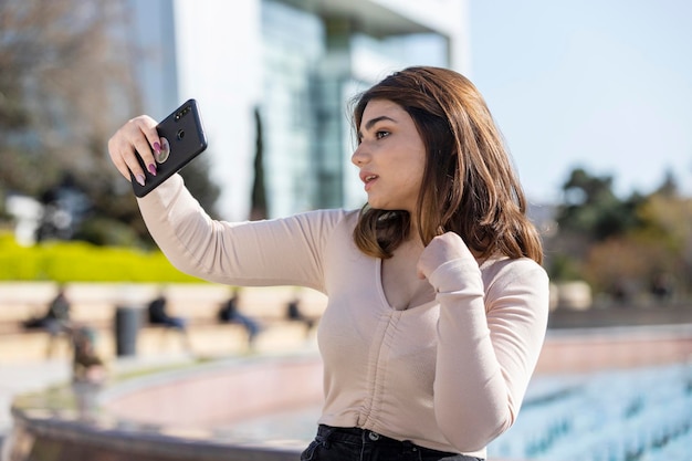 The beautiful young girl sitting at the park and taking selfie High quality photo